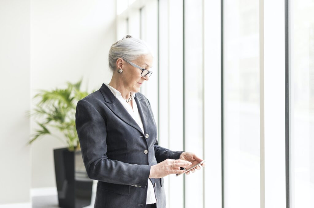 Mature businesswoman looking at smartphone by office window